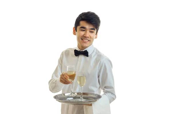 Vrolijke man ober in uniform en bowtie met glazen witte wijn op een zilveren dienblad glimlachen — Stockfoto