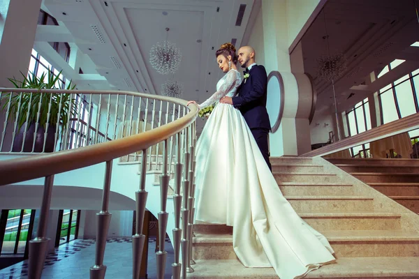 Junges frisch verheiratetes Paar in Hochzeitskostümen, das sich auf einer Leiter umarmt — Stockfoto