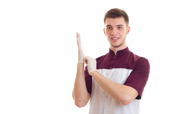 Lächelnder junger Arzt zieht Handschuhe über die Hände und schaut in die Kamera aus nächster Nähe — Stockfoto