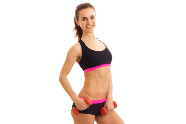 A svelte young fitness girl with beautiful waist smiling looks at the camera and holding a dumbbell — Stock Photo, Image