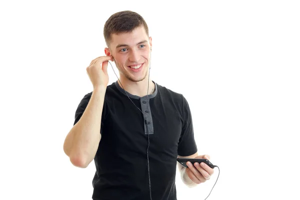 Joyful handsome guy inserts earphones into your ears and listen to music from your phone — Stock Photo, Image