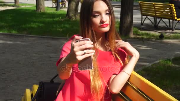 Cutie mladá blonďatá dívka s červenými rty díky selfie v parku — Stock video