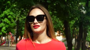 Yakışıklı genç kadın güneş gözlüğü kırmızı dudaklar ile açık havada yürür
