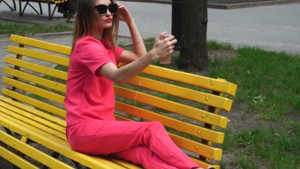 Young beautiful lady on high heels in red suit makes selfie on a bench — Stock Video