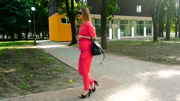 Hermosa chica de negocios joven en traje rojo y gafas de sol camina por la calle en tacones altos — Vídeos de Stock