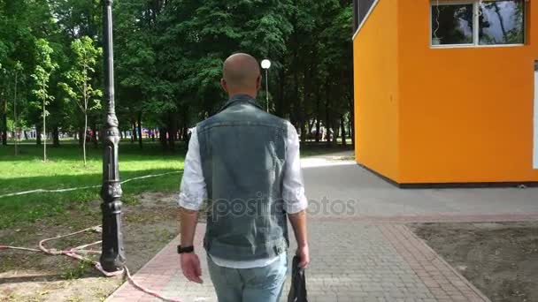 Νεαρό όμορφος άνδρας στο τζιν ρούχα με μαύρη δερμάτινη τσάντα στο χέρι του — Αρχείο Βίντεο