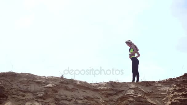 Mladá štíhlá sportovní blondýna v sportovní unform, Pózování na písečném kopci — Stock video