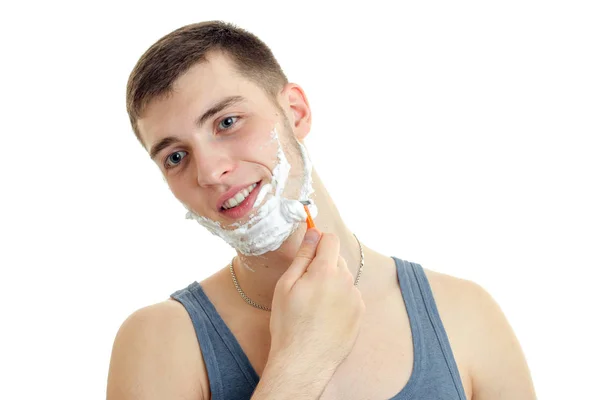 Close-up portrait of a young cute guy with foam on his face who shaves his beard and smiling — Stock Photo, Image