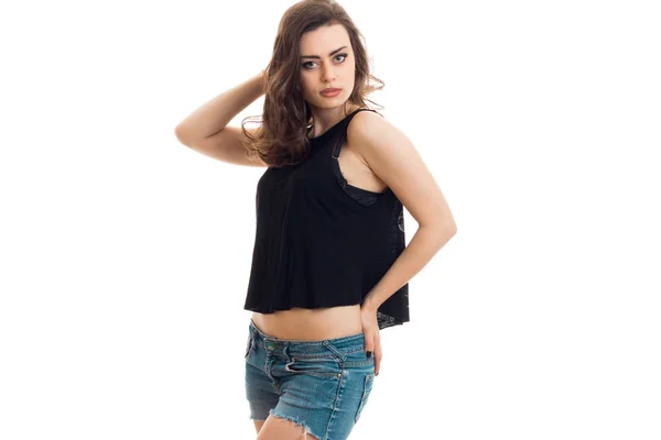 Beautiful young girl in a black t-shirt and shorts holding a hand near the hair and posing for the camera — Stock Photo, Image