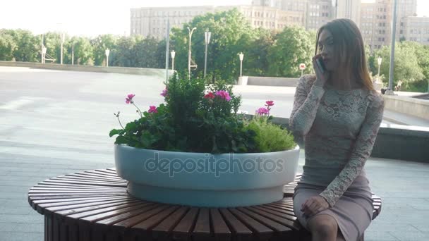 Menina em terno de negócios senta-se ao ar livre e fala telefone celular — Vídeo de Stock