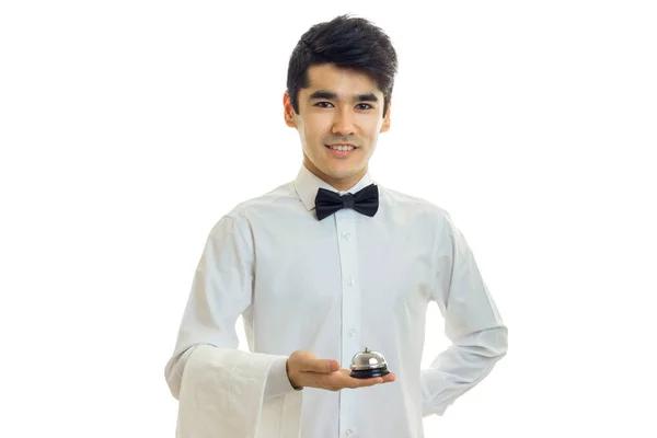 Захоплюючий молодий офіціант посміхається і тримає в руці дзвінок для гостя — стокове фото