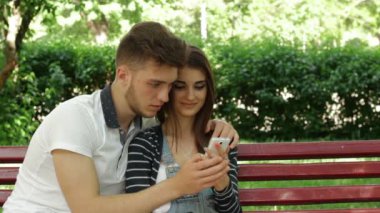 bir bankta oturan ve telefon resimleri izlerken kadın ve erkek