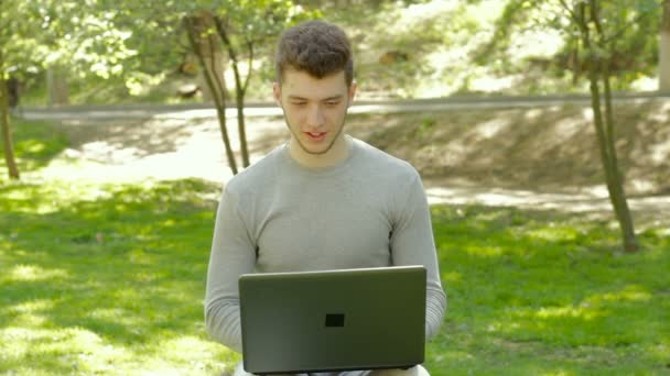Молодой парень-фрилансер работает с ноутбуком в парке — стоковое видео