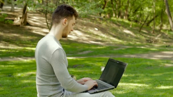 Парень в парке работает с ноутбуком — стоковое видео