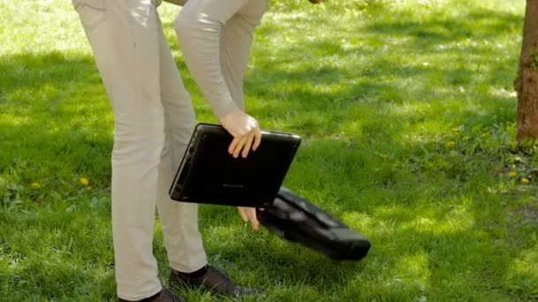 Tipo en el parque se sienta en la hierba en el parque y trabaja con el ordenador portátil — Vídeos de Stock