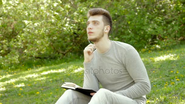 Thoughtful young man make notes in book in the park — Stock Video