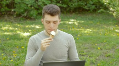 adam parkta bilgisayarla çalışır ve dondurma yiyor
