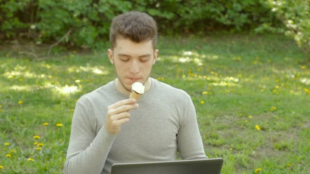 Cara no parque trabalha com computador e come sorvete — Vídeo de Stock