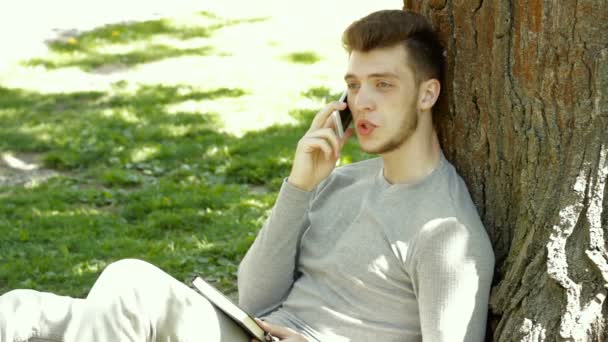 Man in het park onder een boom praten op mobiele telefoon — Stockvideo