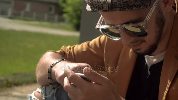 Hombre guapo utiliza un phoen móvil al aire libre — Vídeos de Stock