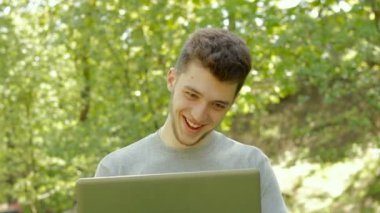 genç gay adam gülümsüyor ve Park içinde belgili tanımlık laptop ile çalışır