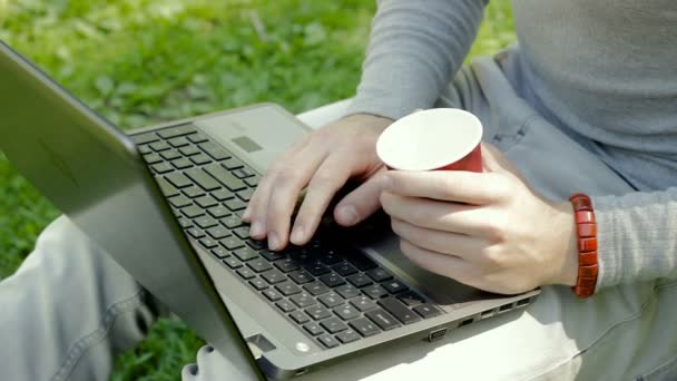 Chico escribe en un ordenador portátil y bebe café — Vídeo de stock