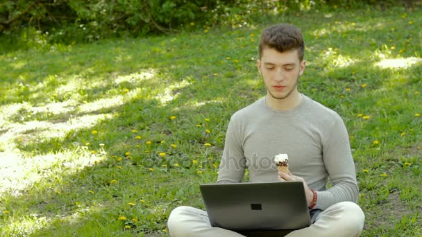 Seriös ung student fungerar med laptop och äta glass i parken — Stockvideo