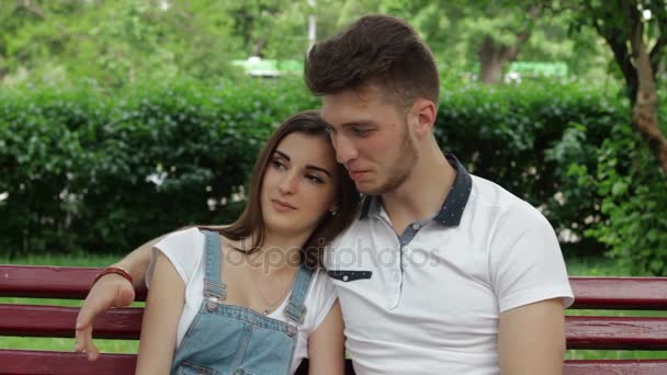 Linda pareja joven abrazándose y hablando en un banco en el parque — Vídeo de stock