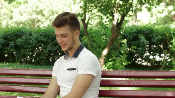 Fille fait surprise son petit ami et ferme les yeux dans le parc sur un banc — Video