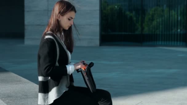 Menina sentada ao ar livre ao vento e trabalha com tablet móvel — Vídeo de Stock