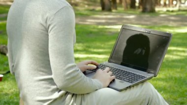 genç adam parkta bir dizüstü bilgisayarda yazıyor