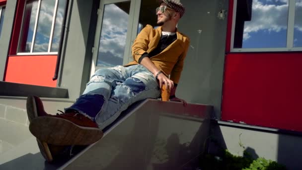 Гламурный модельер в CAP и очки, сидящие на лестнице — стоковое видео