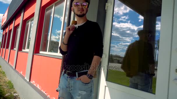 Стильний молодий чоловік в сонцезахисних окулярах виділяється на відкритому повітрі і дивиться в сторону з курткою на плечі — стокове відео