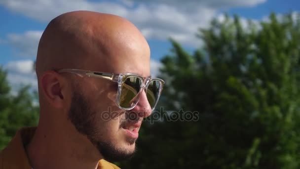 Cara bonito com uma barba e óculos de sol brilhantes coloca em uma cabeça Cap — Vídeo de Stock