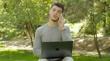dizüstü bilgisayarda çalışan ve parkta telefonda konuşurken öğrenci
