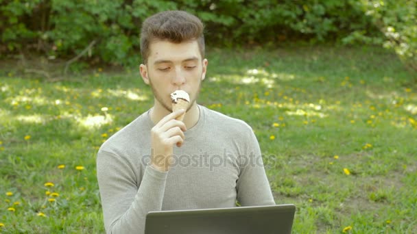 Jovem no parque comer sorvete e trabalha com laptop — Vídeo de Stock