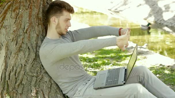 Student w parku pod drzewem zgina palce i sprawia, że notatki w notesie — Wideo stockowe