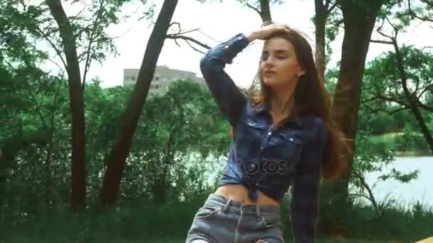Menina atraente sentado em um banco no parque e o vento agita seu cabelo — Vídeo de Stock