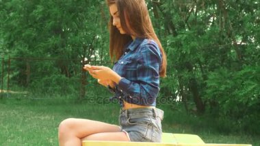 Genç Kız parkta ve bir cep telefonu kullanarak bir bankta oturur