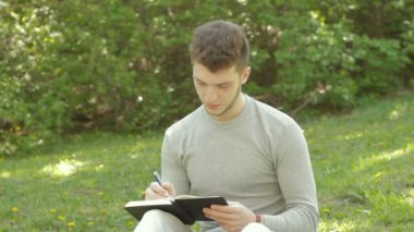 yakışıklı adam parkta çim üzerinde oturur ve kitapta notlar