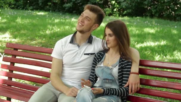 Guy with girl talk in the Park on a bench and using mobile phone — Stock Video