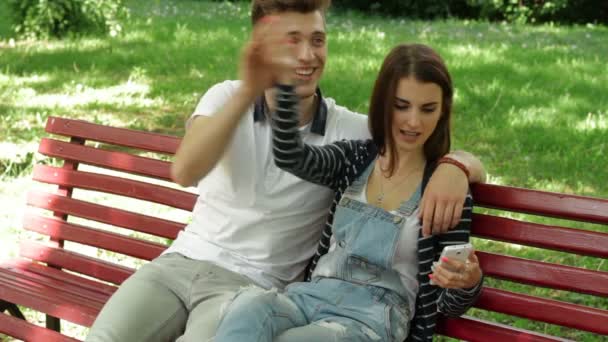 Парень смотрит фотографии своей девушки на скамейке в мобильном телефоне — стоковое видео