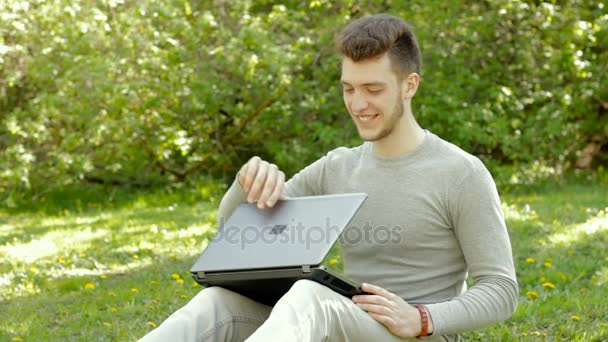 Vrolijke jongeman opent een laptop op het park en verrast glimlacht — Stockvideo