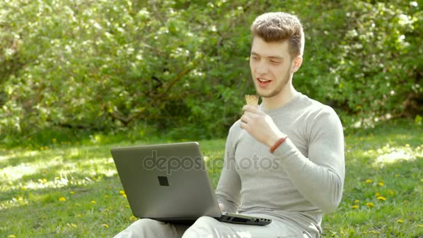 Facet z laptopem wideo mówi i zjada lody w parku — Wideo stockowe