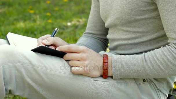 Guy makes notes in a Notepad in the Park — Stock Video