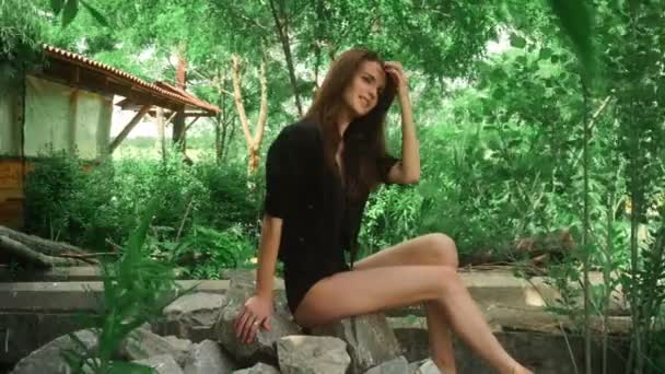 Εύθυμος μελαχρινή κοπέλα κάθεται πάνω στο βράχο στο πάρκο και άνεμος ανακατεύει τα μαλλιά — Αρχείο Βίντεο