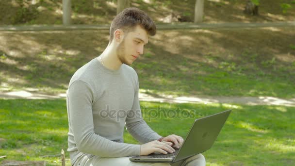 Молодой симпатичный мужчина в парке работает с ноутбуком — стоковое видео