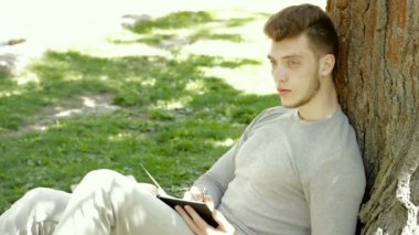 Genç öğrenci ağacın gölgesinde oturur ve notlar