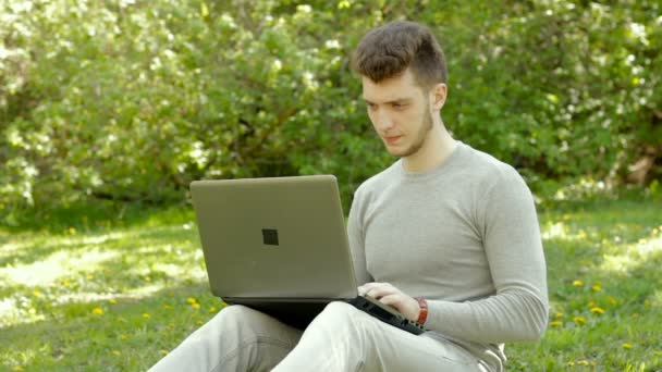 Joven freelancer serio que trabaja con el ordenador portátil al aire libre — Vídeos de Stock