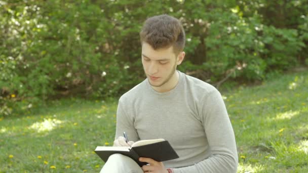 Σοβαρές νεαρός φοιτητής κάνετε σημειώσεις στο πάρκο — Αρχείο Βίντεο